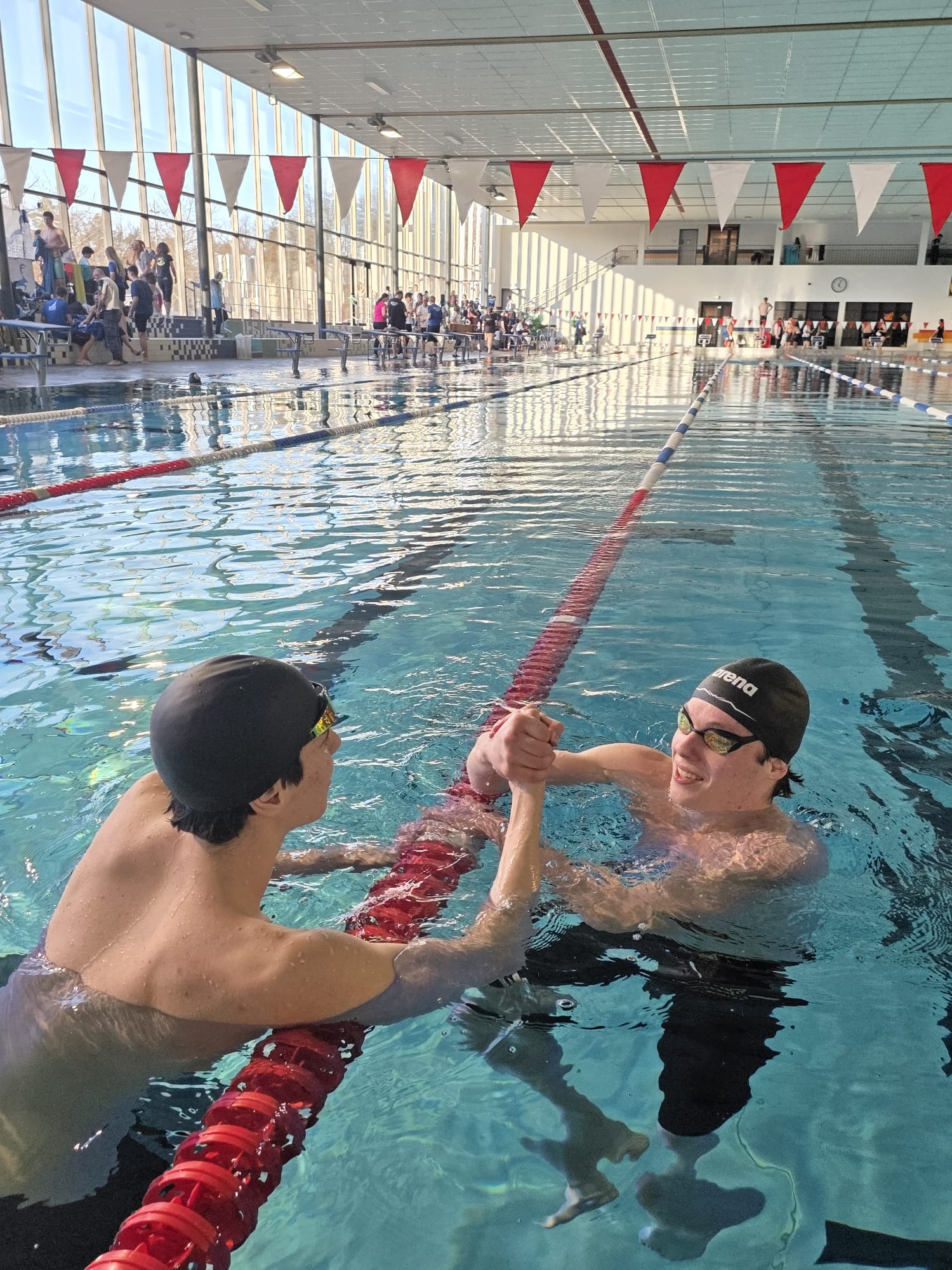 Zwei Schwimmer reichen sich im Wasser die Hände